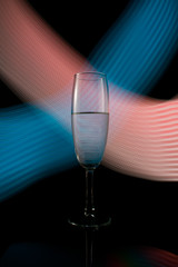 A single wine glass isolated on a black background with red white pink and orange neon light painting streaks of light behind them. Light wave, game of colors, drawing light.