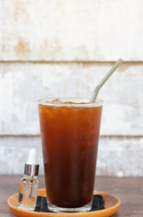 Coffee ice americano with additional syrup bottle for customer.  Ice black tea in high glass with canvas coaster.