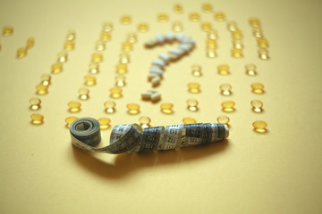  centimeter tape and question mark of pills on a colored background with space for text. concept of losing weight, diet, fat burning, healthy eating.