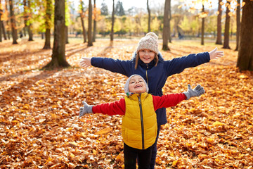 childhood, season and people concept - happy children on fallen leaves at autumn park