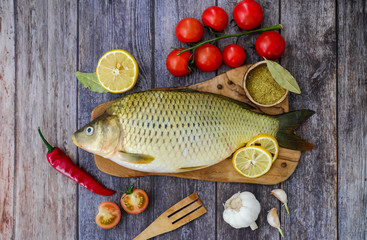 Carp on a wooden kitchen Board surrounded by lemons, spices, greens. Fish ready to cook.