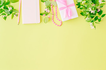 Flat lay blogger or freelancer workspace with a notebook, gift box, branches and green leaves on a green background