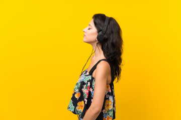 Young woman over isolated yellow background listening to music with headphones