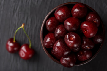 Ripe and juicy cherry berries on a black textural background in a brown cup, with water drops. Top view, close-up.