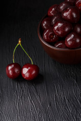 Ripe and juicy cherry berries on a black textural background in a brown cup, with water drops. Top view, close-up.