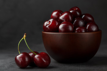 Ripe and juicy cherry berries on a black textural background in a brown cup, with water drops. Top view, close-up.