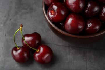 Ripe and juicy cherry berries on a black textural background in a brown cup, with water drops. Top view, close-up.