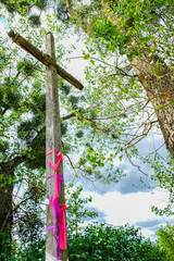 Obraz premium Old wooden high cross with pink ribbons on the background of the sky. Bottom view. The disappearing village of Svalovichi in Ukraine. Ukrainian Polissya