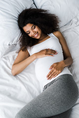 top view of smiling pregnant african american woman lying on bed