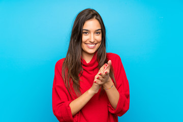 Young woman with red sweater over isolated blue background applauding