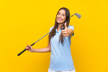 Young golfer woman over isolated yellow wall with thumbs up because something good has happened
