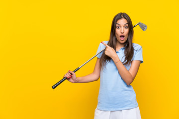 Young golfer woman over isolated yellow wall surprised and pointing side