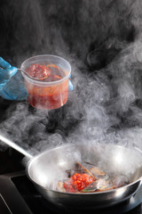 Cook adds tomato sauce in midi flambe. Concept of cooking in public, food show. Catering business....