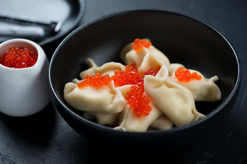 Closeup of vareniki or dumplings with cottage cheese and addition of red caviar served in a black bowl, studio shot