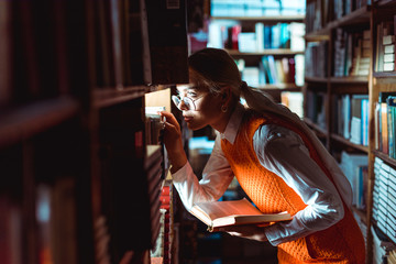 pretty woman in glasses looking away and holding book in library