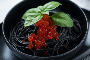 Closeup of spaghetti with squid-ink, red caviar and fresh green basil, selective focus