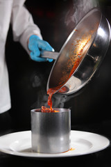 The cook spreads the cooked mussels to the flambé from the pan in the form on a white plate. Food...