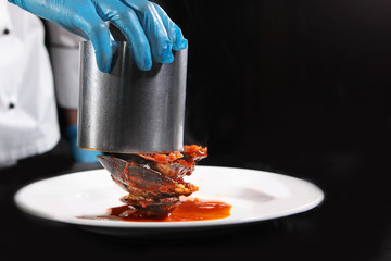 The cook spreads the cooked mussels to the flambé from the pan in the form on a white plate. Food...