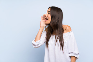 Young woman over isolated blue background shouting with mouth wide open