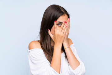 Young woman over isolated blue background covering eyes and looking through fingers