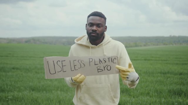 Serious young african american man holds a poster use less plastic bro look at camera portrait tree field forest volunteering charity ecology agriculture care environment spring organic slow motion