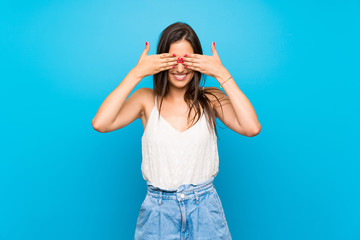 Young woman over isolated blue background covering eyes by hands