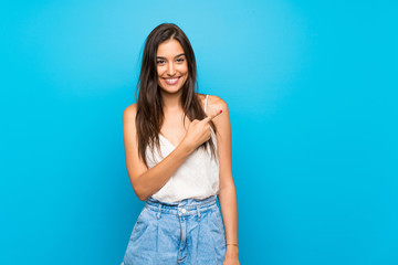 Young woman over isolated blue background frightened and pointing to the side