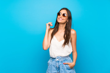 Young woman over isolated blue background with glasses and smiling