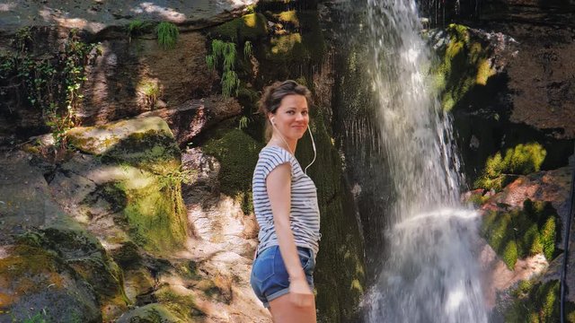 Young woman dancing in front of waterfall.