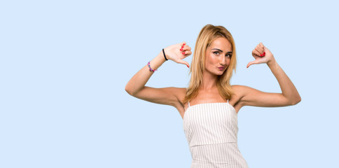 Young blonde woman showing thumb down over isolated blue background