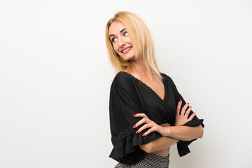 Young blonde woman over isolated white wall with arms crossed and happy