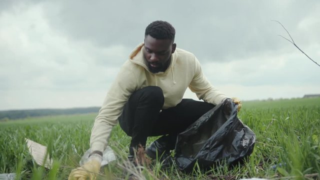 African american man volunteer gathering plastic bottles in garbage bag ecology nature pollution rubbish care charity volunteering community environment young altruism recycle slow motion