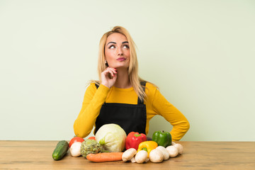 Fototapeta premium Young blonde woman with lots of vegetables thinking an idea