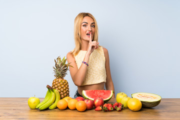 Young blonde woman with lots of fruits doing silence gesture