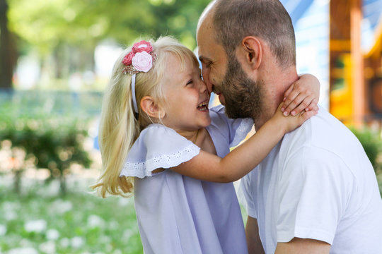 Happy father and daughter spending time together in a park on a summer day and warmly hugging each other.