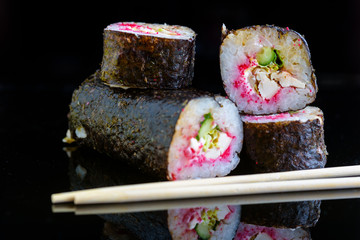Sushi rolls on a black mirror background.