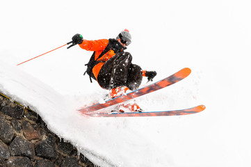 The athlete skier on a light background with a jump moves off the roof of a snow-covered hut with flying flakes of snow. The concept of winter ski sports