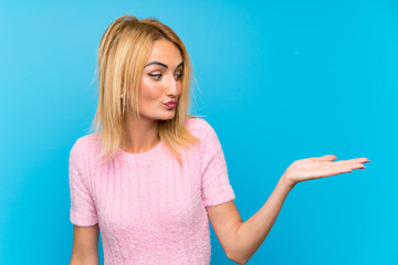 Fototapeta premium Young blonde woman over blue background holding copyspace imaginary on the palm