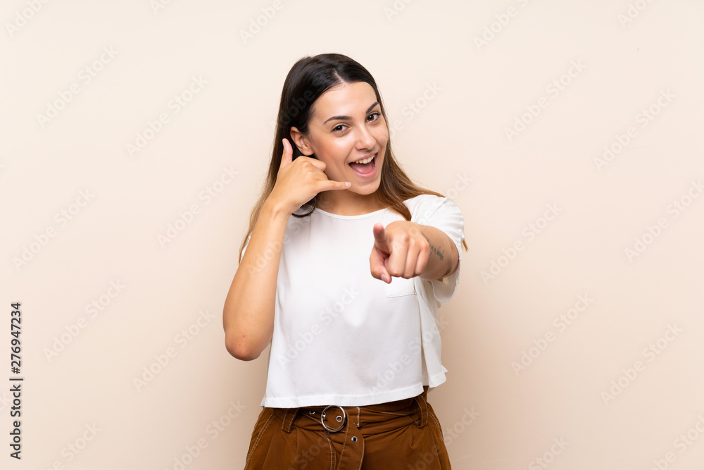 Wall mural young brunette woman over isolated background making phone gesture and pointing front