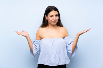 Young brunette woman over isolated blue background having doubts with confuse face expression