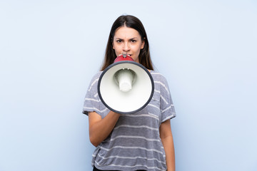 Young brunette woman over isolated blue background shouting through a megaphone