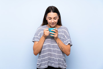 Young brunette woman over isolated blue background holding hot cup of coffee