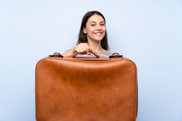 Young brunette woman over isolated blue background holding a vintage briefcase