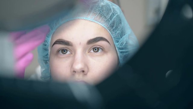 cosmetologist hands put special eyebrow ruler on client face to check applying permanent makeup at mirror