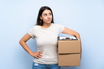 Young delivery woman over blue brick wall making doubts gesture while lifting the shoulders