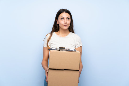 Young delivery woman over blue brick wall looking up while smiling