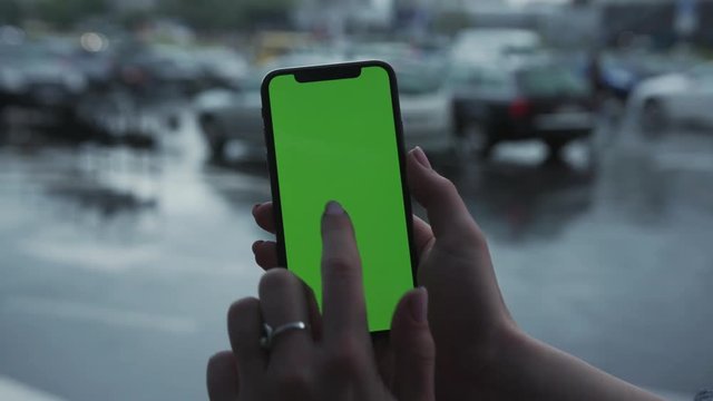 Los Angeles, California - 5 April 2019: Close-up woman hand holding use vertically smart phone cellphone green screen background rain parking cars weather app cellphone outside rain trees raindrops
