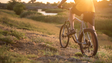 Cyclist riding the bike down rocky hill at sunset. Close up extreme sport concept	