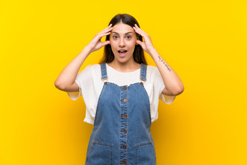 Young woman in dungarees over isolated yellow background with surprise expression