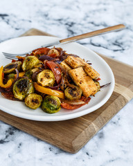Front view of plate with roasted tofu and vegetables: brussels sprouts, bell peppers, tomatoes and red onions